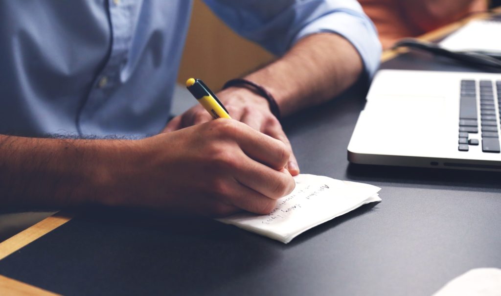 Imagem de um homem escrevendo em um bloco de notas, fazendo alusão a um planejamento de atividades. Fonte: Pixabay